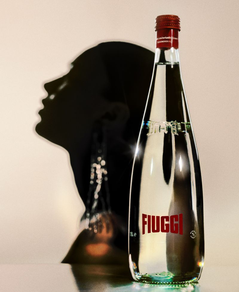 A bottle of Fiuggi mineral water stands in front of a shadowy silhouette of a woman's profile, highlighting the product's refined presentation.