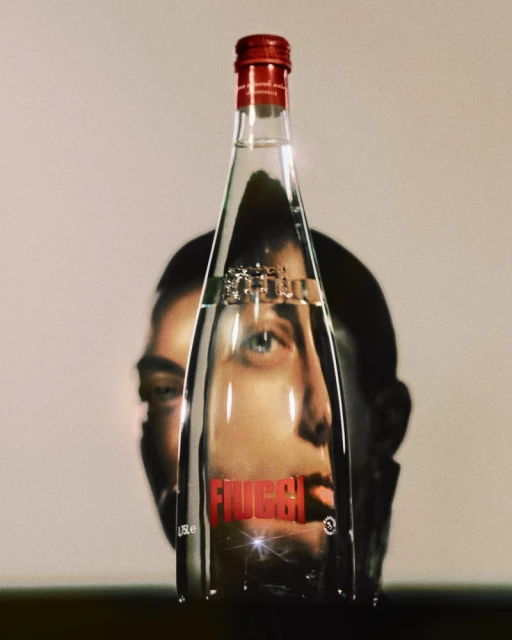 Bottle of Fiuggi water with a red cap reflecting a human face against a plain background with studio lighting. Food and beverage.
