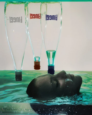 A person's face submerged in water with three glass bottles hanging upside down above them for Vogue Italia by Elizaveta Porodina