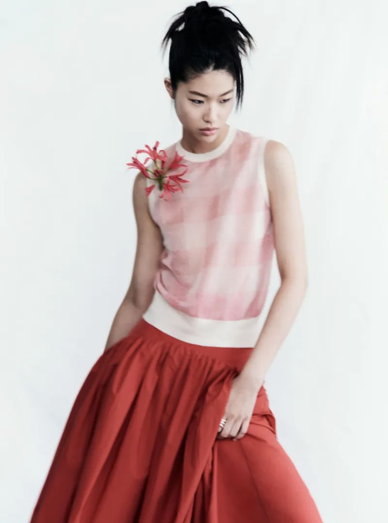 Asian woman in a sleeveless top and a red skirt with a flower detail, posing in front of a white background in a fashion-style portrait.
