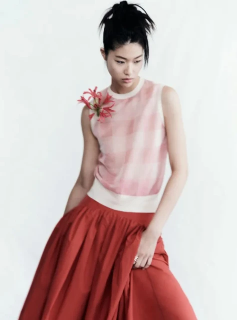 Asian woman in a sleeveless top and a red skirt with a flower detail, posing in front of a white background in a fashion-style portrait.