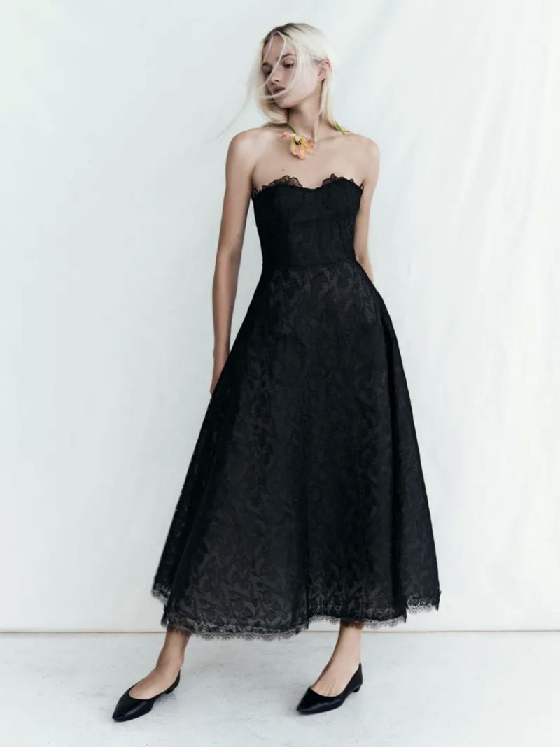 Model wearing a black strapless lace midi dress against a plain white studio background