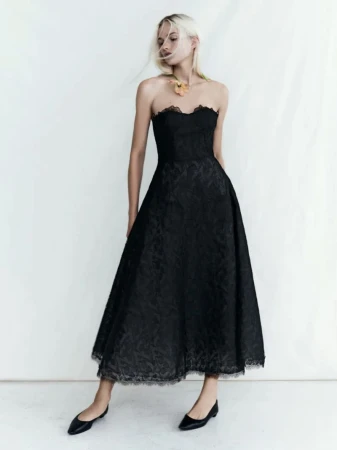 Model wearing a black strapless lace midi dress against a plain white studio background