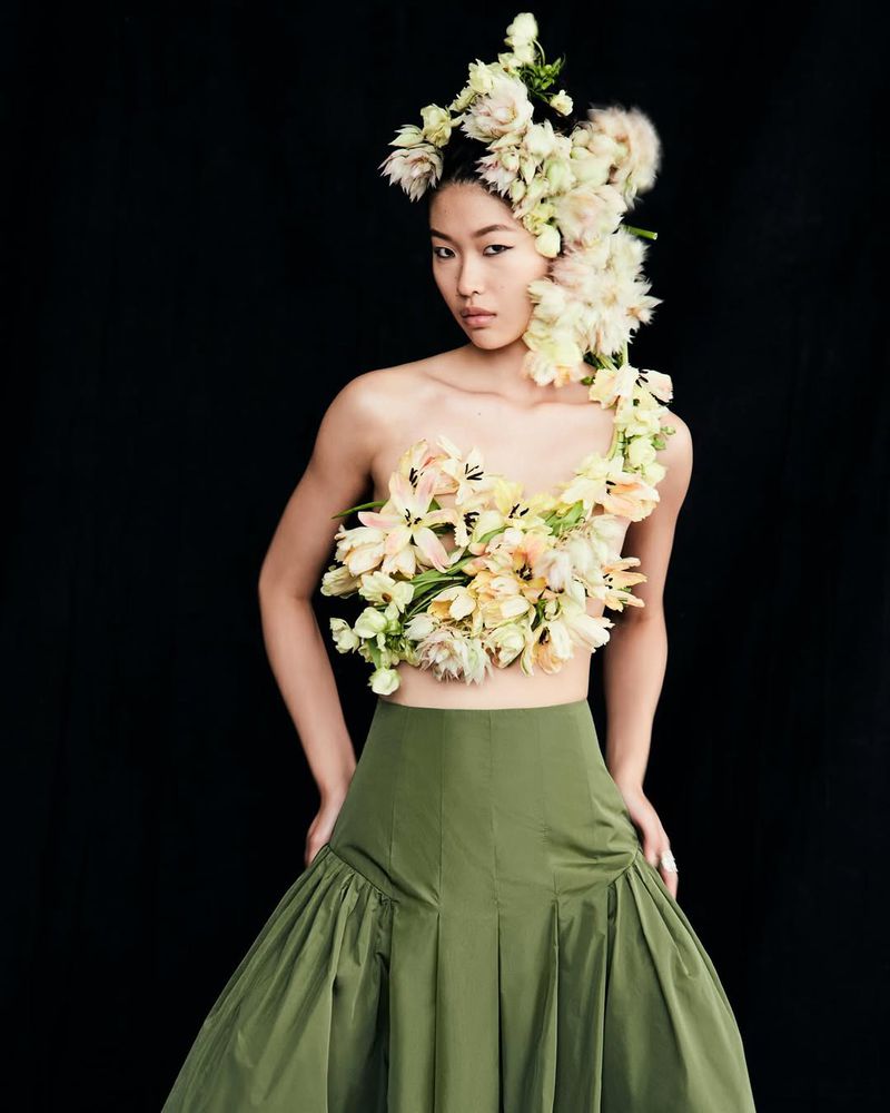 Striking studio portrait of an Asian woman in a green skirt, adorned with a crown and bodice of vibrant cream and yellow flowers.