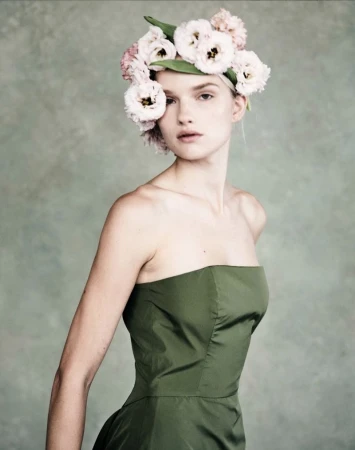Woman wearing a green strapless dress and a floral headpiece poses in front of a mottled grey and green background in a studio portrait.