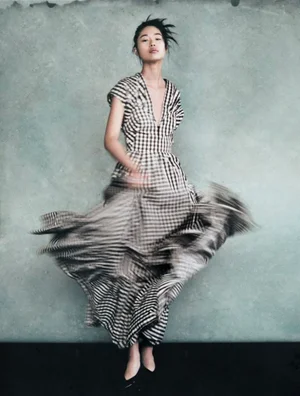 Model in a black and white gingham maxi dress twirling against a textured grey studio backdrop