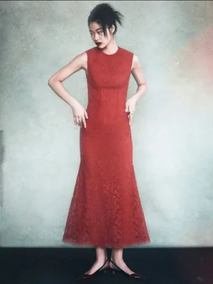 Model wearing a sleeveless red lace midi dress and black slingback shoes against a textured neutral background