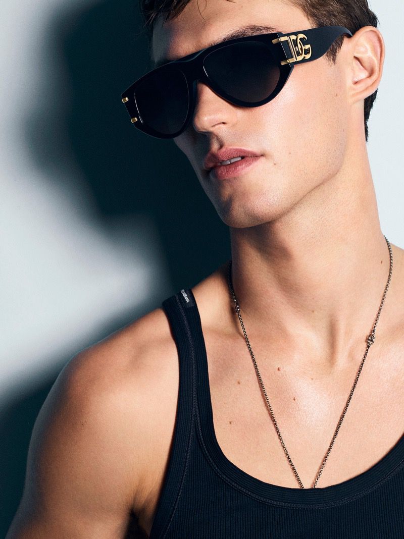 Close-up of a man wearing black tank top and sunglasses. The sunglasses have gold accents. He is also wearing a gold chain.