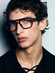 Close-up portrait of a young man wearing black thick-framed eyeglasses against a neutral studio backdrop for Dolce and Gabbana.