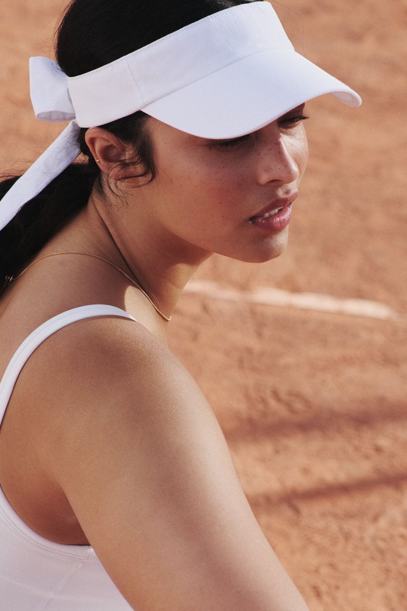 Portrait of a brunette woman wearing a white visor, posing on a tennis court, with a close-up shot showcasing natural light.