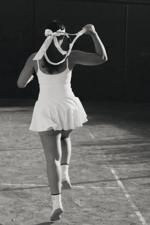 Model wearing a white tennis dress and visor holding a racket on a court