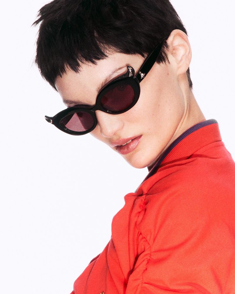 Model wearing dark sunglasses and an orange top against a plain white background for Vivienne Westwood