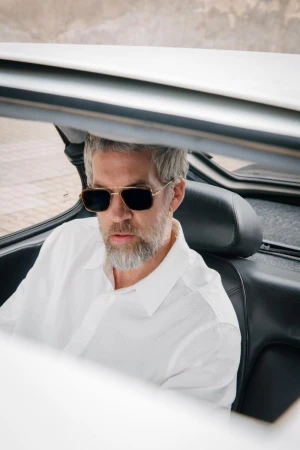 Man wearing sunglasses and a white shirt seated inside a classic car for Atlant Eyewear campaign.