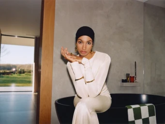 Model Ikram Abdi Omar sitting on a black bathtub wearing a white top and black cap for the Selfridges Eid Campaign 2025.