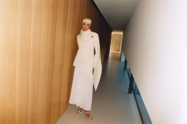 Model Ikram Abdi Omar wearing a white suit and matching hijab in a modern hallway for Selfridges Eid Campaign 2025