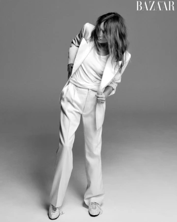 Carla Bruni wearing a white suit and t-shirt against a grey studio backdrop in a black and white editorial portrait.