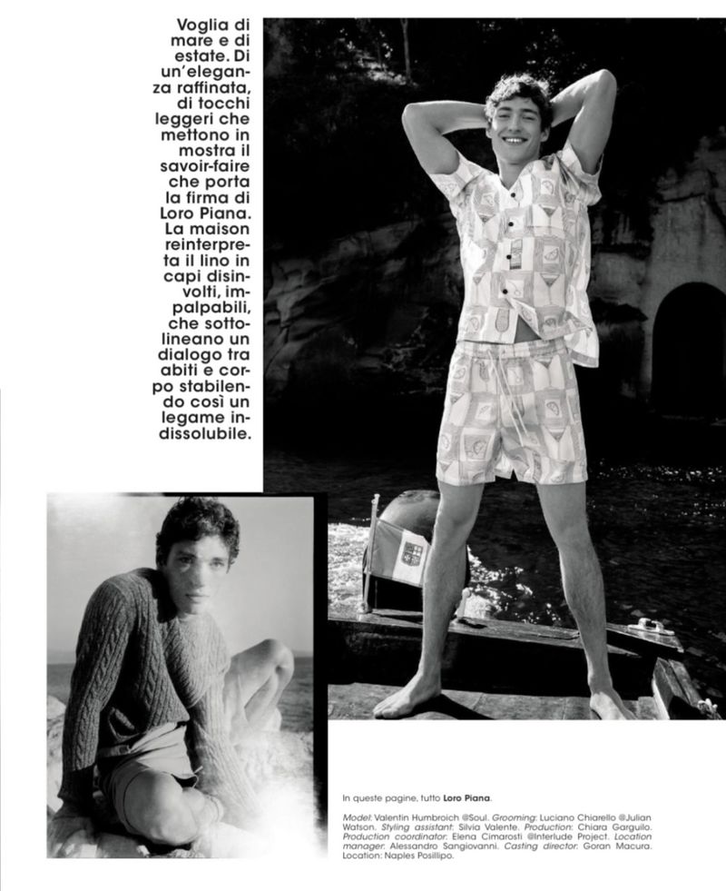 Monochrome fashion shot featuring a young adult male model in a patterned linen shirt and shorts by a rocky shoreline.