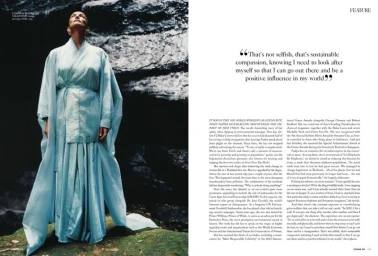 Model wearing a light blue belted wrap dress standing outdoors against dark textured stone rocks