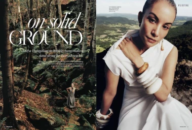 Woman wearing a white dress and stacked chunky bangles posing outdoors against a lush green forest landscape