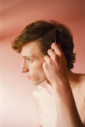 Close-up portrait of a young man combing his brown hair against a plain pink background for a Schön Magazine editorial.