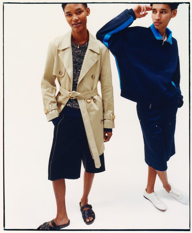 Two male models posing against a white background, one wearing a beige trench coat and the other in a navy blue tracksuit top