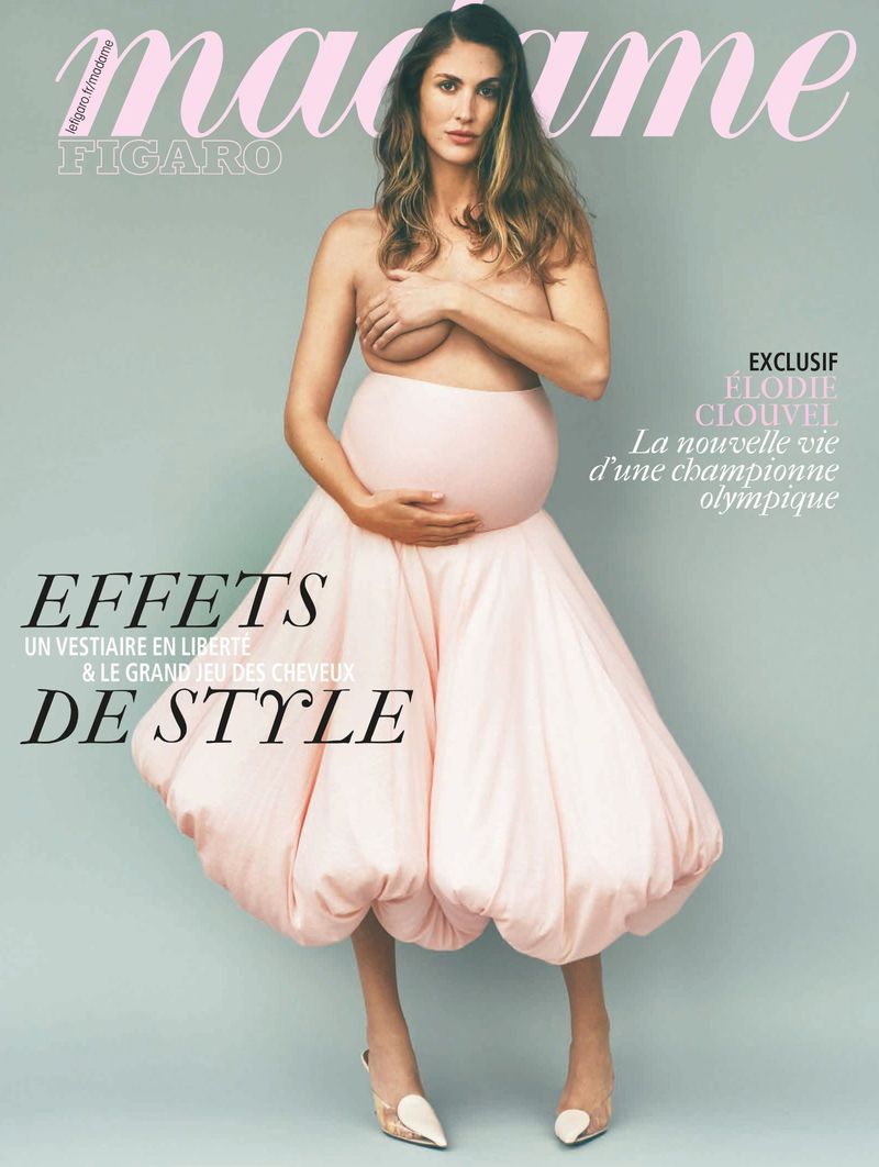 Magazine cover featuring a pregnant woman with long hair, partially nude, wearing a pink skirt and high heels against a light-blue background.