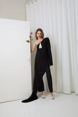 Fashionable woman in black dress and pants, white heels, and holding a pink rose, poses in front of a white door and curtain.