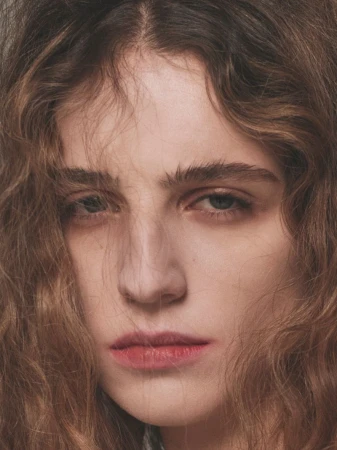 Close-up portrait of a young woman with wavy brown hair framing her face and soft natural lighting.
