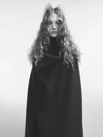 Model with long wavy hair wearing a dark coat against a white background for Beyond Noise project by Willy Vanderperre