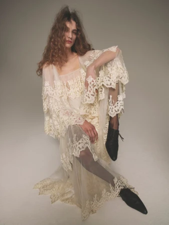 Model Lota Blaskovic in cream lace dress and black lace-up shoes seated against a plain neutral backdrop.