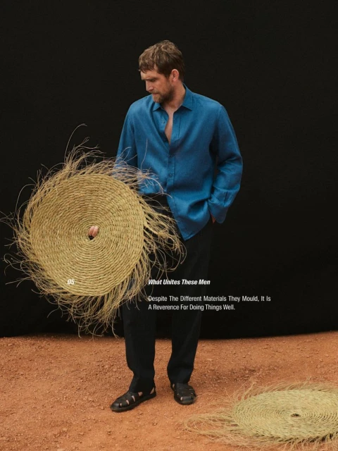 An adult man in a blue shirt holds a woven straw circle. The subject stands in front of a black background with a terracotta surface.