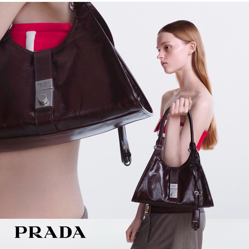 Fashion shot of a brunette model holding a brown leather Prada handbag against a white background in a vertical studio shot.