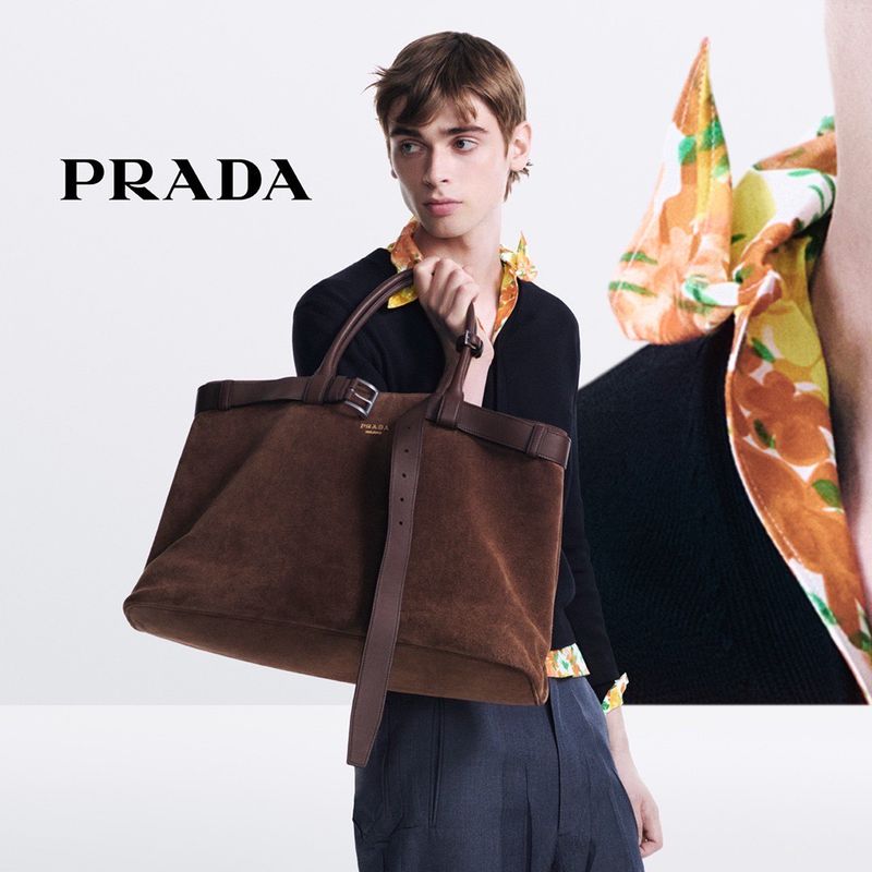 A model poses with a brown Prada suede tote bag in a fashion shot. The image features the Prada logo and a partially visible floral scarf.