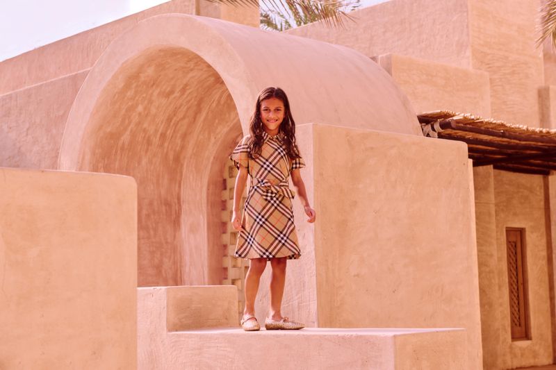 Young girl in plaid dress smiles on architectural steps in warm sunlight. Fashion shot with desert environment in the background.