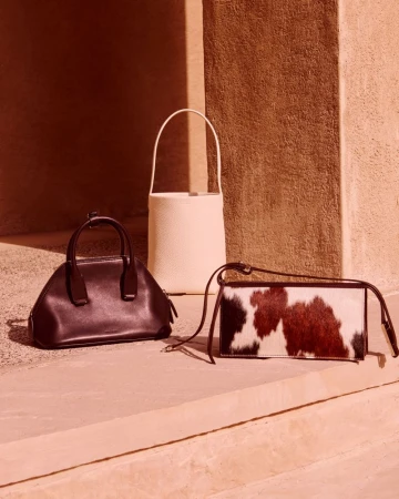Three luxury designer handbags displayed on stone surfaces against a warm architectural background for Harvey Nichols Dubai.