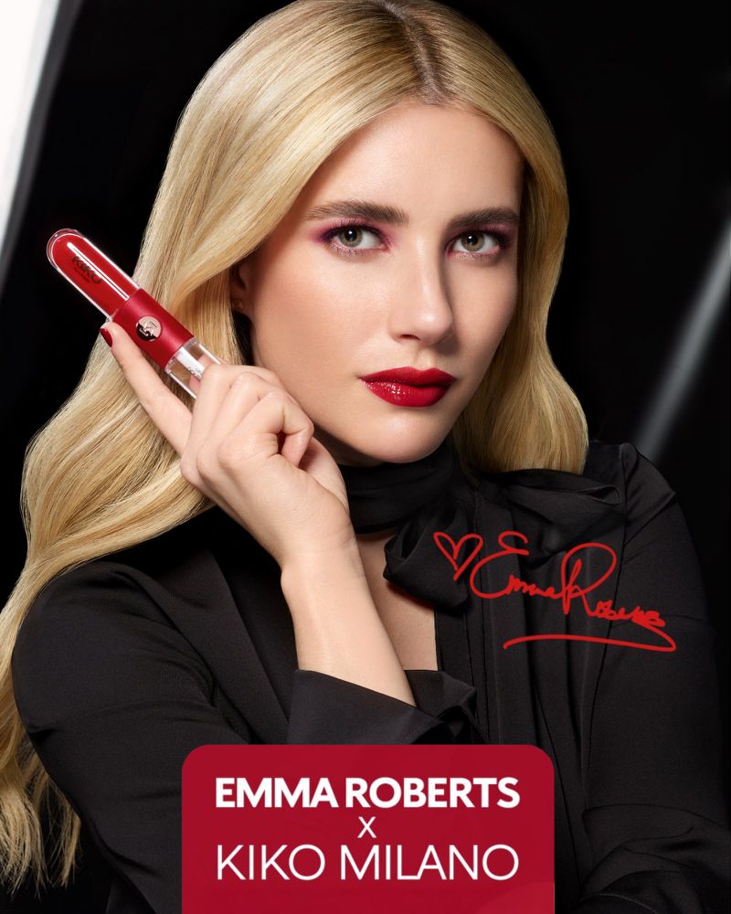 Emma Roberts poses with red Kiko Milano lipstick against a black backdrop, modeling makeup from the beauty brand’s promotional campaign.