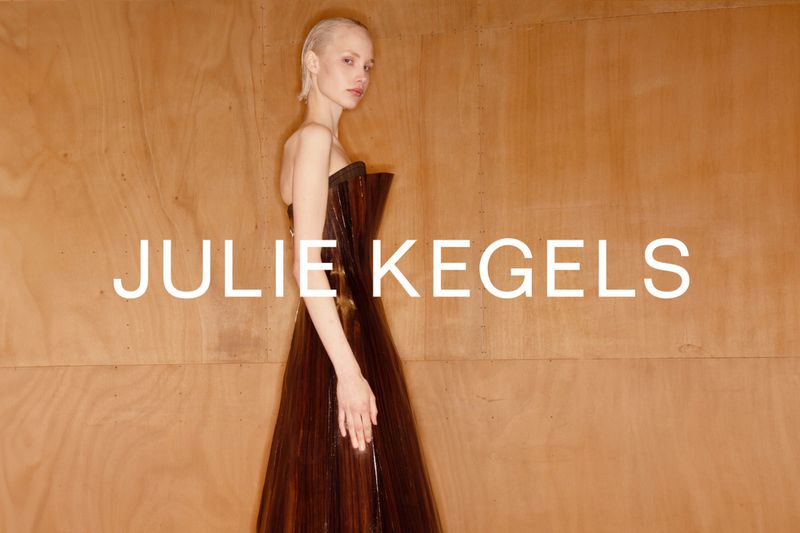Fashion portrait of a woman in a dark dress against a wood background with the white text overlay of "JULIE KEGELS."