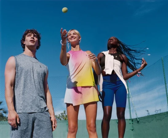 Three models looking up at a tennis ball against a clear blue sky on an outdoor court for On Running.