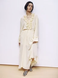Model in cream ruffled blouse and matching skirt against a white studio background
