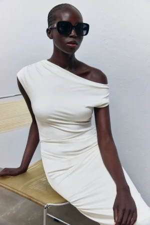 Model Ajok Madel wearing a white dress and sunglasses seated on a woven chair for BOSS