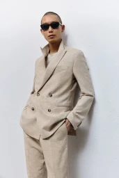 Model wearing a beige double-breasted suit and dark sunglasses posing against a plain white background for BOSS
