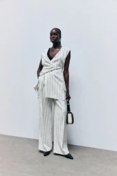 Model Ajok Madel wearing a striped vest and matching trousers holding a handbag against a white studio wall