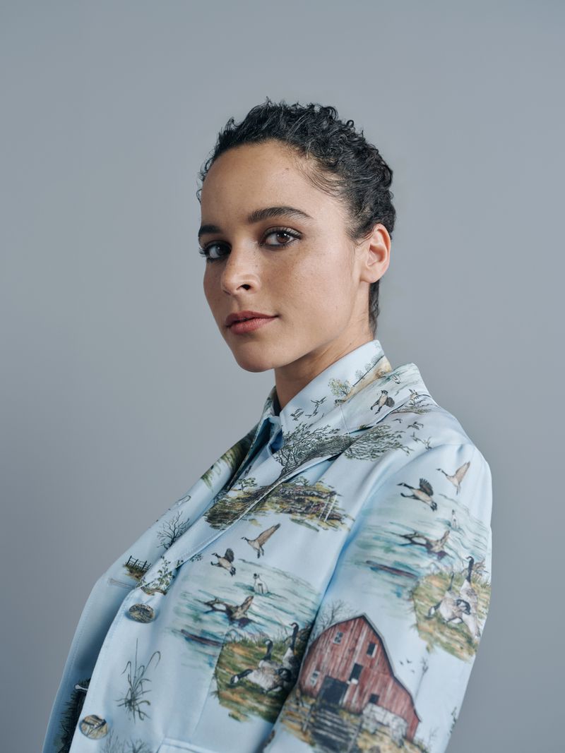 Portrait of a woman with dark hair wearing a blazer with a detailed outdoor landscape print against a light gray backdrop.