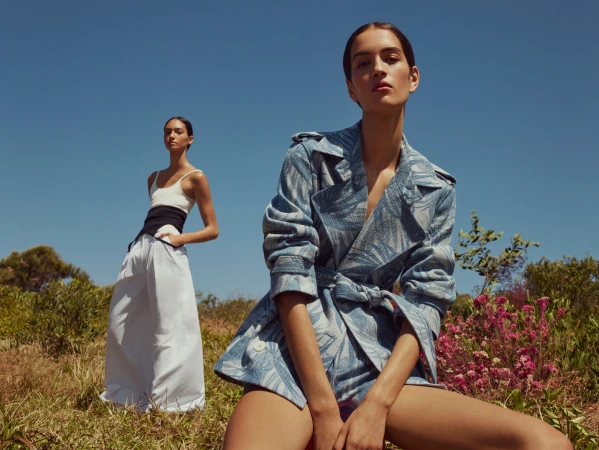 Two female models posing outdoors in a grassy landscape under a clear blue sky for a Scanlan Theodore campaign