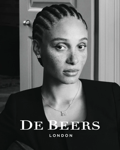 Black-and-white portrait of Adwoa Aboah wearing diamond jewelry and a black top against an interior doorway.