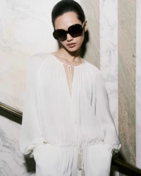 Model wearing dark sunglasses and a white long-sleeve top against a marble-patterned wall for Tom Ford SS25