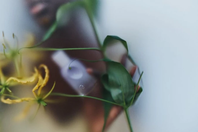 Close-up of yellow flowers and green leaves with a cosmetic bottle in the background, creating a serene, natural beauty aesthetic.