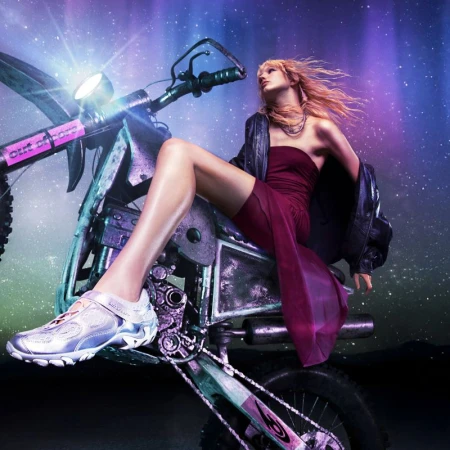 Model in a magenta dress and dark jacket seated on a metallic dirt bike against a purple starry night sky background