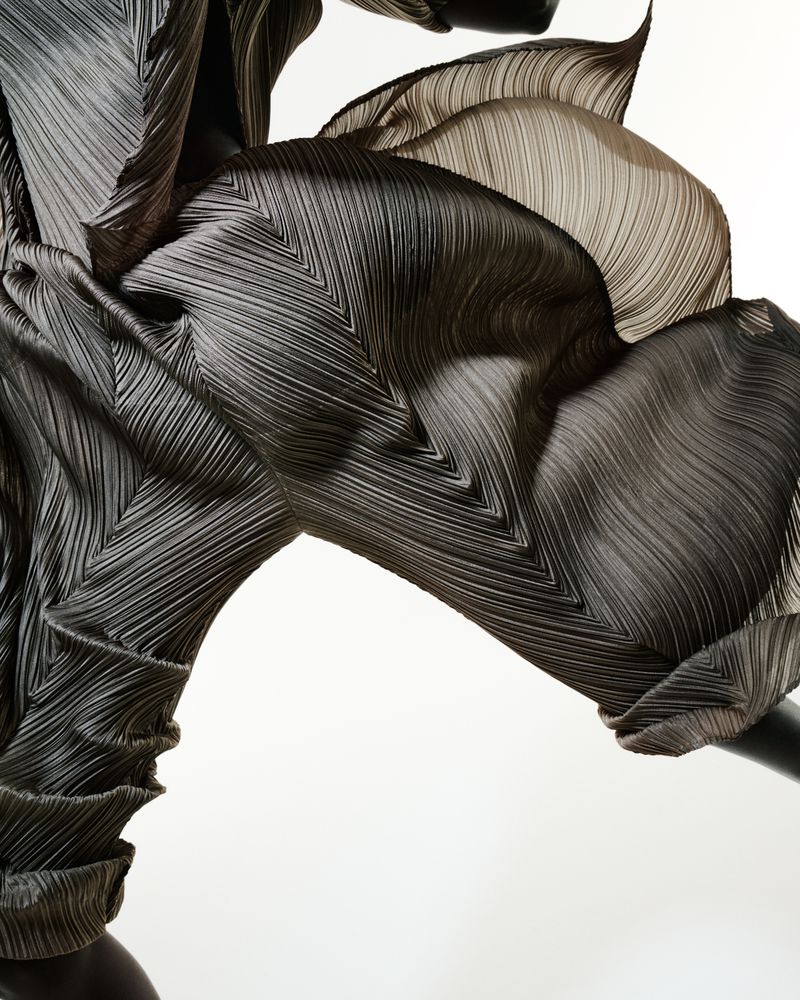 Abstract fashion photograph featuring textured and pleated sculptural garment with black and tan coloring against a stark white backdrop.