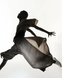 Model mid-air wearing pleated clothing against a stark white studio background
